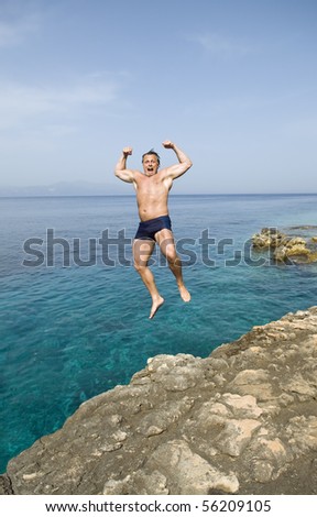 A color portrait photo of a man jumping into the sea while flexing his muscles.
