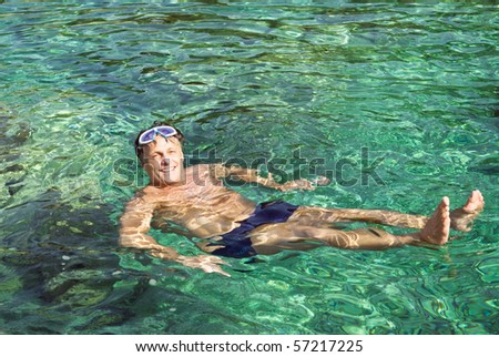 A happy smiling man in his forties floating in the beautiful turquoise water of the ionian sea in Greece.