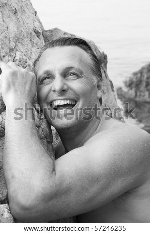 A black and white portrait of a happy laughing sexy man in his forties having fun at the beach.