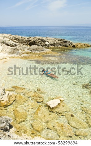A beautiful asian woman floating in the stunning blue turquoise water of the ionian sea in Paxos Greece.