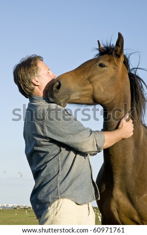 A handsome forties man is petting his beautiful brown horse.