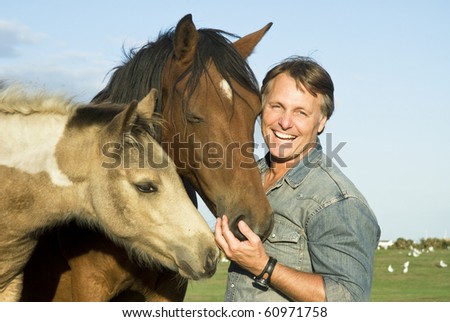 A color portrait photo of a handsome smiling man petting his beautiful horses.
