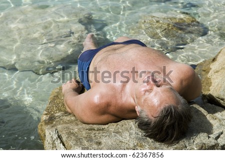 A caucasian man sunbathing on some rocks in Paxos Greece.