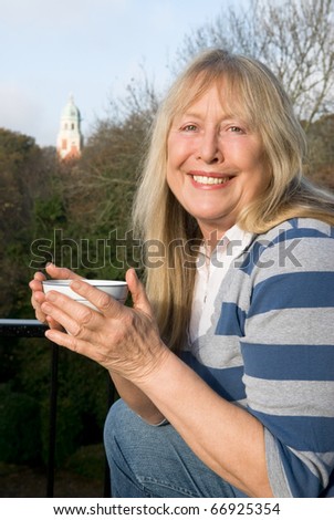 A happy smiling woman in her sixties holding a cup of coffee and looking at the camera.