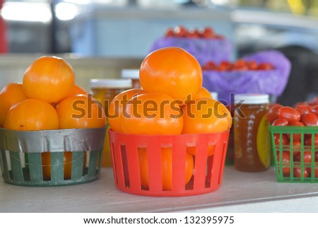 Baskets of orange tomatoes for sale at a roadside fruit and vegetable stand.