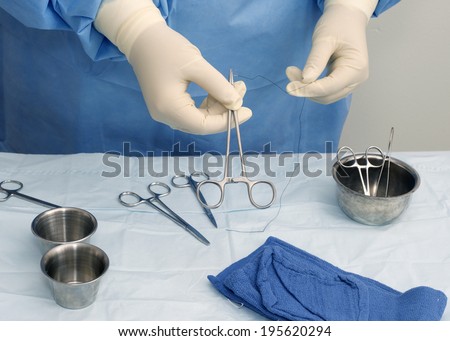 Surgical technician prepares needle holder and suture for use during surgery.