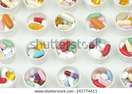 Many different assorted colorful pills in paper medication dosage cups.