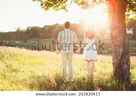 Young happy couple standing on the field, hand in hand, on the sunset