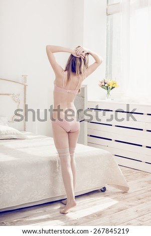 Beautiful woman in white interior  bedroom near the mirror, looking at herself