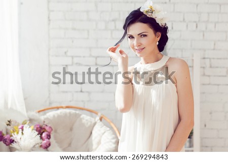 Gorgeous bride with wedding bouquet makeup and hairstyle in bridal dress at home waiting for groom.