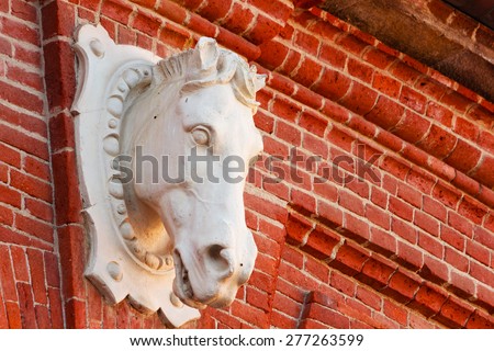 statue of a horse on red brick wall that depicts the shape of the head,to indicate the handling of a horse riding school within a riding club