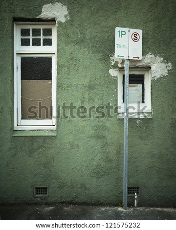 Crumbling, textured green wall with parking sign and windows.
