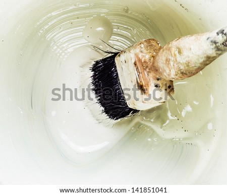 Close-up of an old brush dipped in a swirl of thick white paint at the bottom of a paint can.