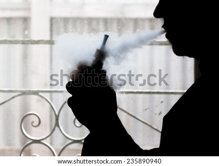 Silhouette of a man using an electronic cigarette (vaping) at home.