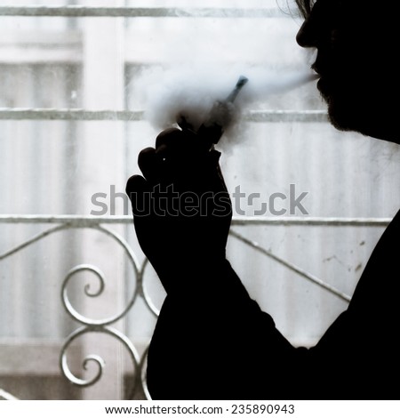 Silhouette of a man using an electronic cigarette (vaping) at home.