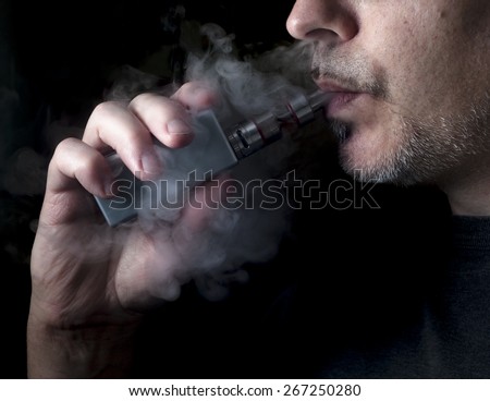 Man using an advanced personal vaporizer or e-cigarette, close up; low-key image.