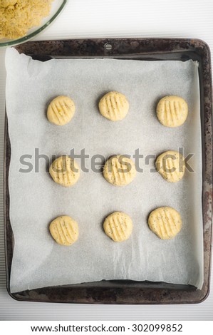 Sweet lemon and poppy seed biscuit dough pressed into shapes on a paper-lined, metal baking tray, ready for the oven.