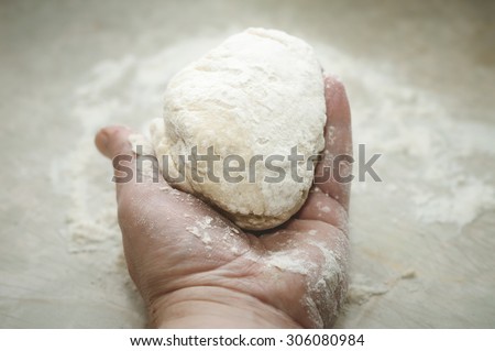Hand holding a ball of homemade bread or pizza dough, ready for kneading.