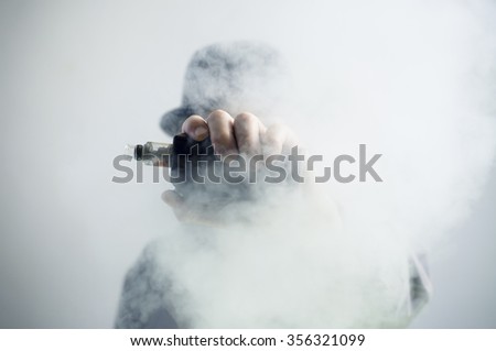 Mysterious vaping man wearing a hat, holding up a mod, obscured behind a cloud of vapor.