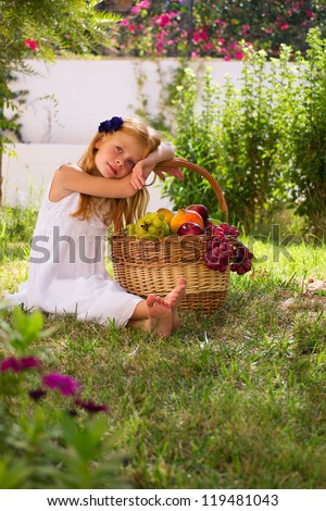 Girl sitting on the grass with a basket of fruit