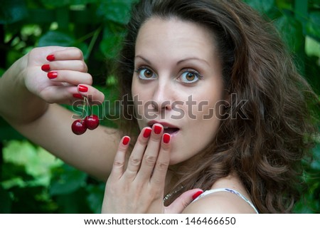 sensual woman eating a cherry on a background of foliage