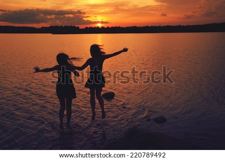 girls jump in the lake at sunset in summer