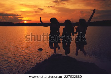 girls jump in the lake at sunset in summer