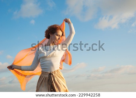 young woman holding a handkerchief in the wind against the sky