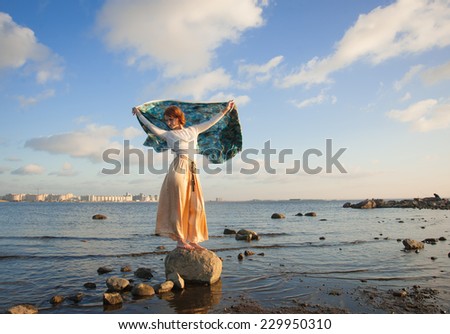 young woman develops a scarf in the wind on the beach