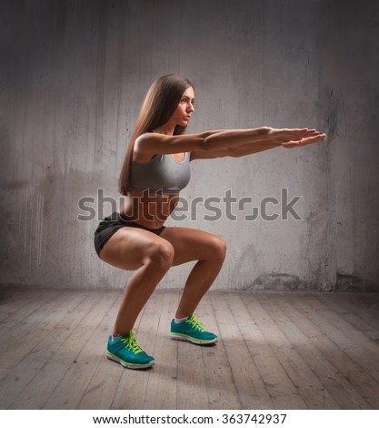 Muscular brunette woman doing squats in brutal interior