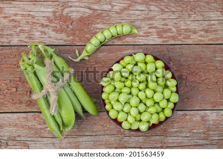 Green peas in a small plate on a wooden background.