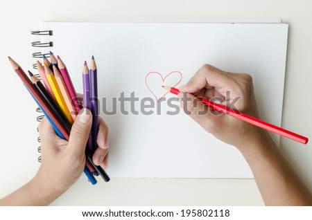 Man holding a fistful of colored pencils in one hand while commencing sketching in a sketch book