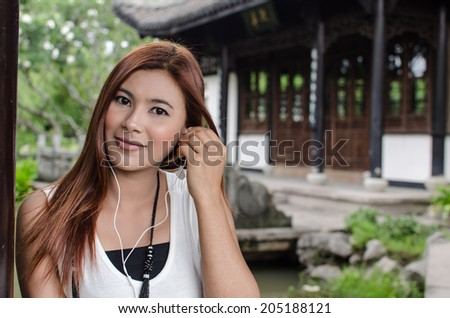 Smiling young woman enjoying her music sitting in the garden wearing ear plugs listening to tunes on her music player