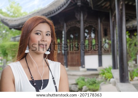 Smiling young woman enjoying her music sitting in the garden wearing ear plugs listening to tunes on her music player