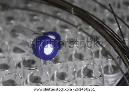 Glass test tubes or containers in a metal rack in an industrial or medical laboratory, view from above with focus to one with a blue stopper