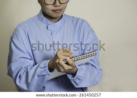 Young female Asian lab worker wearing spectacles writing on the lab notebook