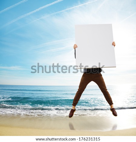 Man jumping on a beach wit blank poster in his hands