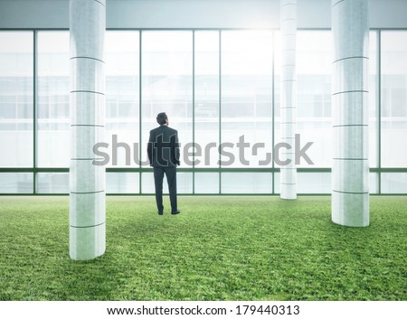 Businessman standing in bright modern office with green grass floor