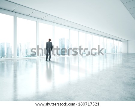 Businessman standing in empty bright office and look at city