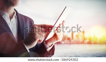 Man with tablet computer and city on horizon