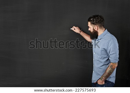 Bearded and tattooed man draws on a chalkboard