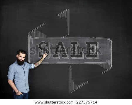 Bearded tattooed man draws SALE on a chalkboard