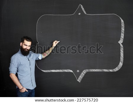 Bearded tattooed man draws frame on a chalkboard