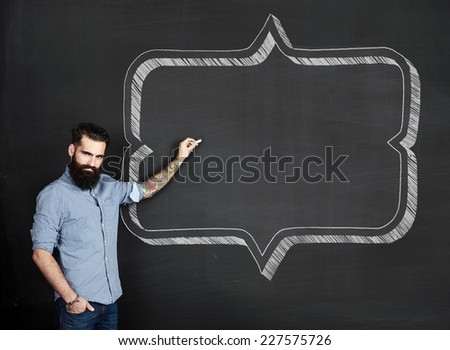 Bearded tattooed man draws retro frame on a chalkboard