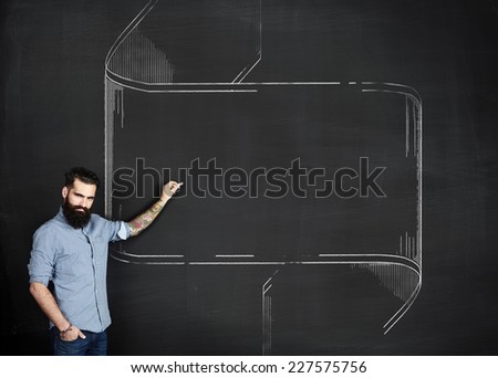 Bearded tattooed man draws vintage frame on a chalkboard