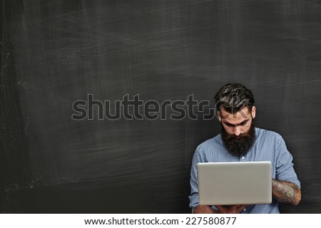 Bearded man with laptop on blank chalkboard background
