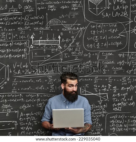 Bearded man with laptop. Chalkboard background with formulas.