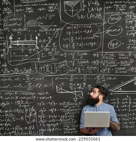 Bearded man with laptop looking at chalkboard with formulas