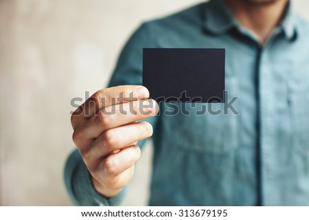 Man holding black business card on concrete wall background