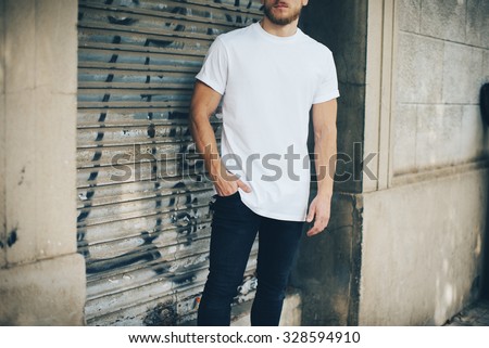 Bearded young man wearing white blank t-shirt and blue jeans, standing on the street